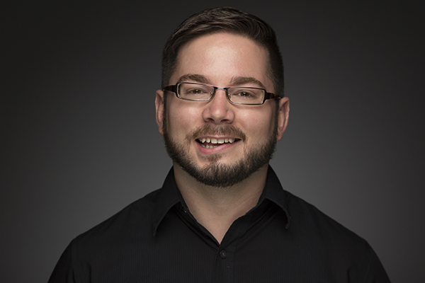 a white dude in glasses with short hair, a moustache and beard, and a black shirt.